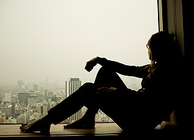 Person sitting by window overlooking cityscape.